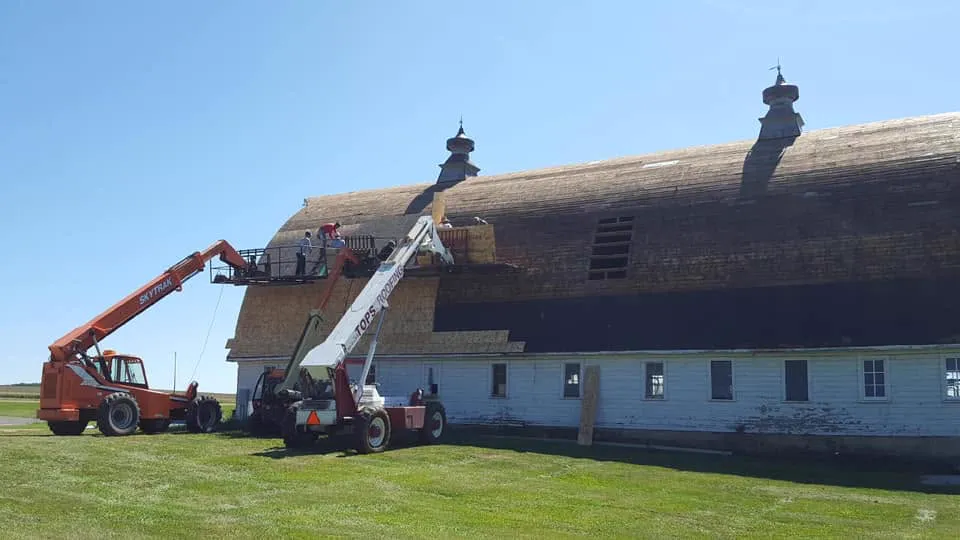 Two boom lifts and a crew redecking a large white barn roof