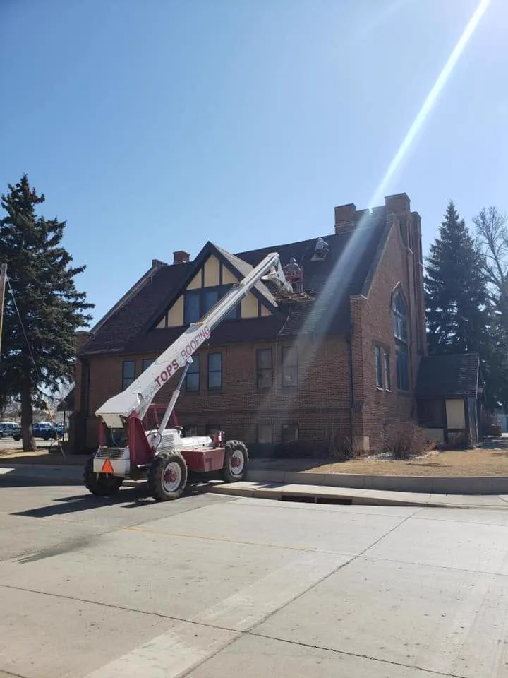 A Tops Roofing boom lift raised to the roof of a brick church