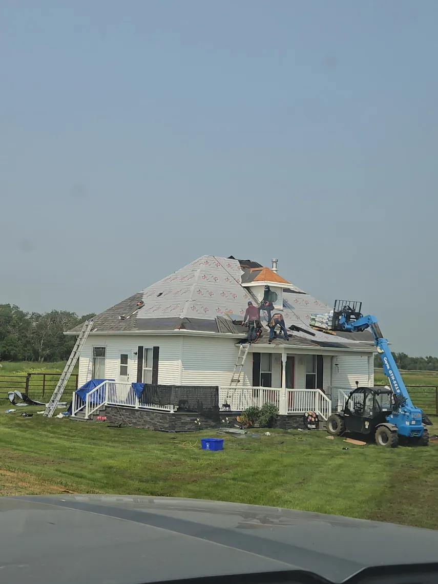 A large white farmhouse mid-reroof with new underlayment installed and a Tops Roofing crew working from a boom lift