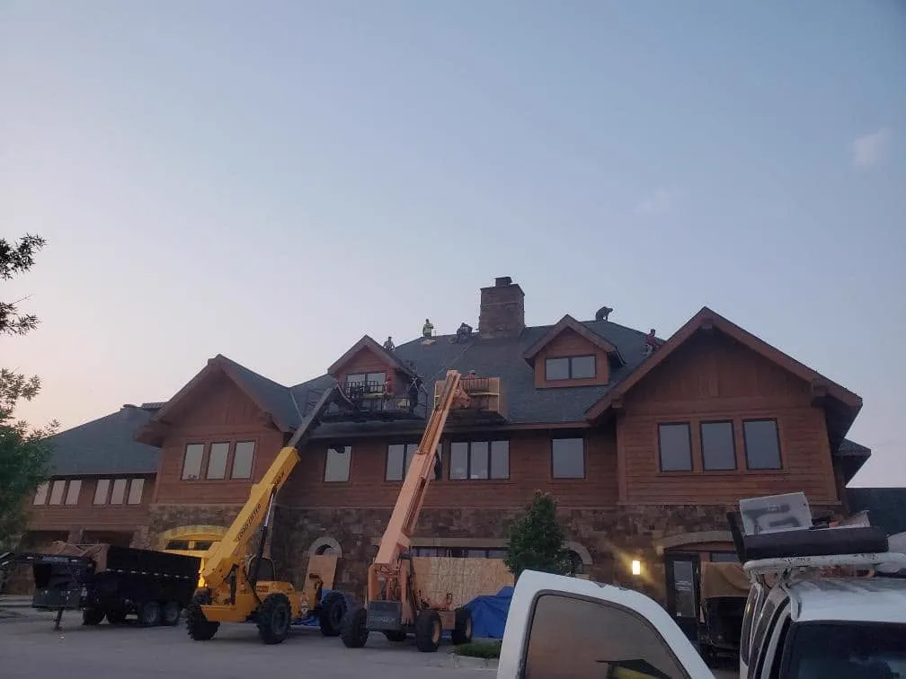 Two boom lifts and a crew reroofing a large log home at dusk