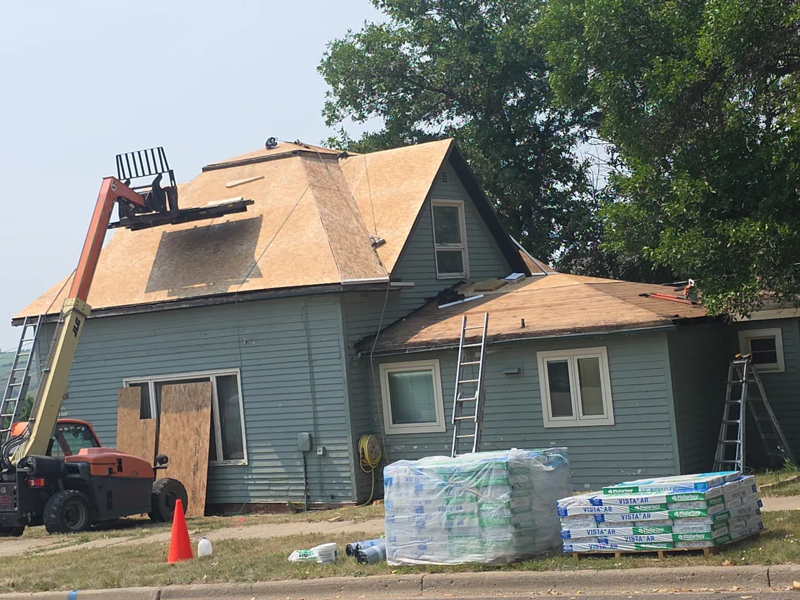 A Tops Roofing crew installing new plywood roof decking on a steep gable roof with shingle bundles staged below