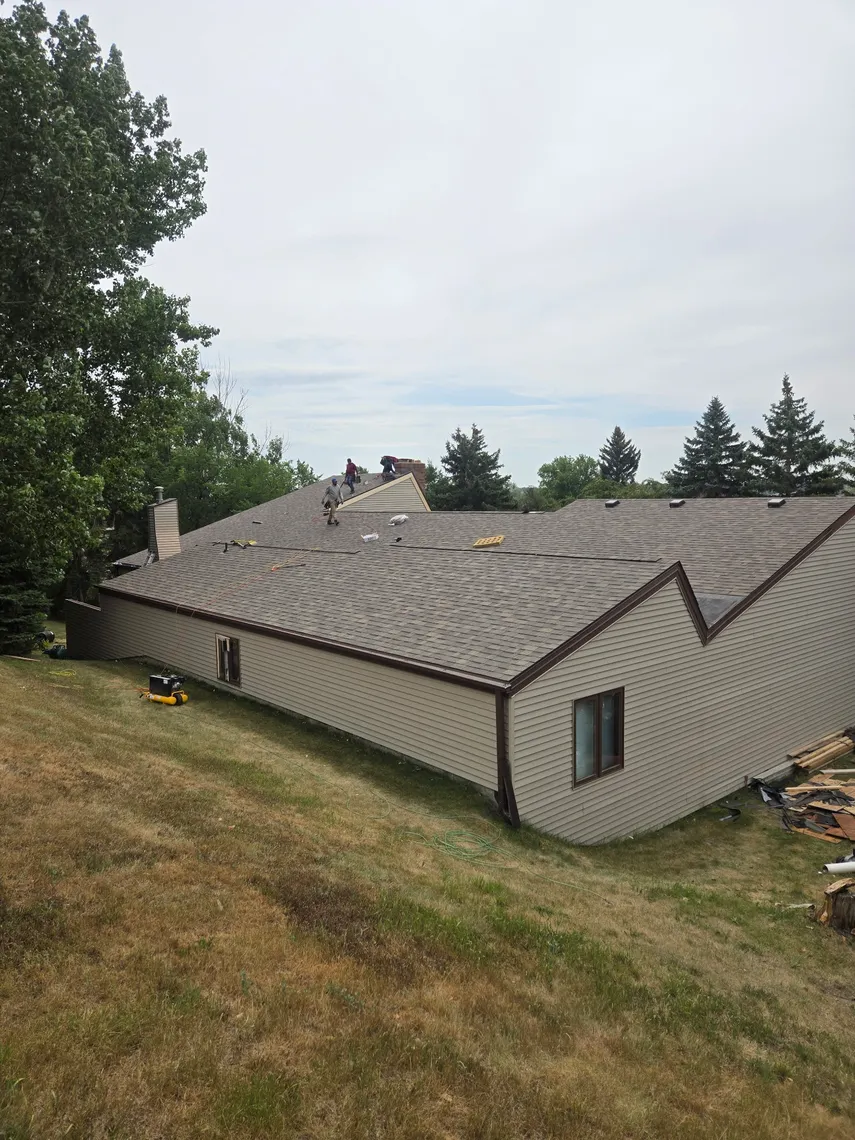 A Tops Roofing crew reroofing a large ranch-style home with multiple gables and a brick chimney