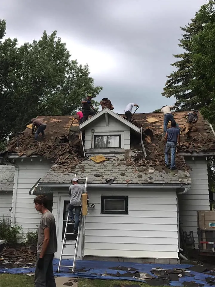 A large Tops Roofing crew tearing off the roof of a white house