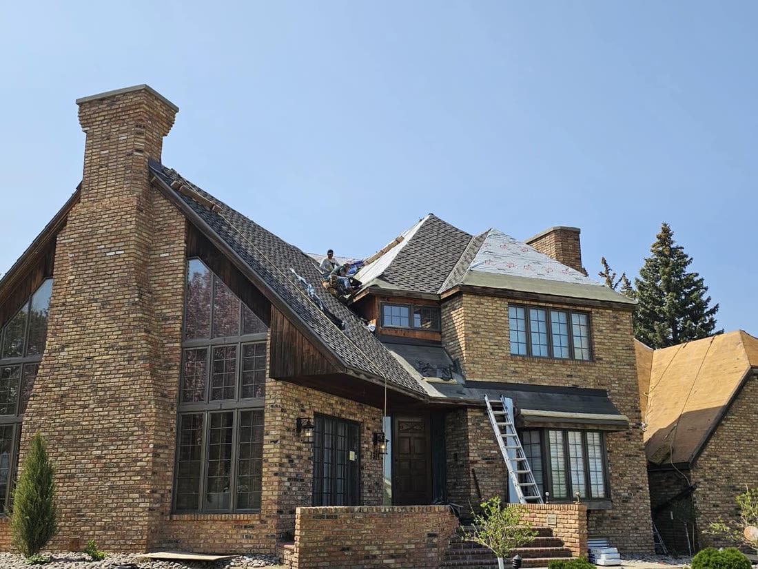 Tops Roofing crew members installing new shingles on a large brick home