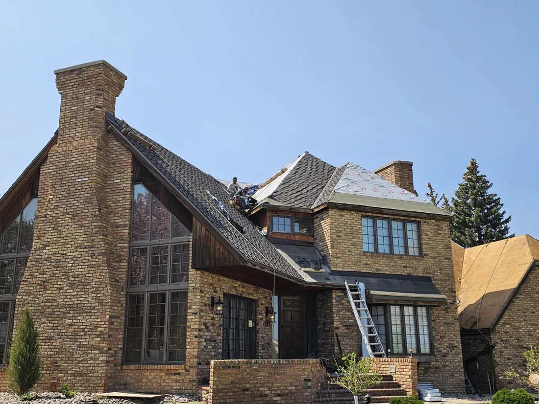 Tops Roofing crew members installing new shingles on a large brick home