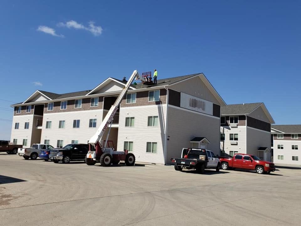 A Tops Roofing crew on a boom lift reroofing a three-story apartment building