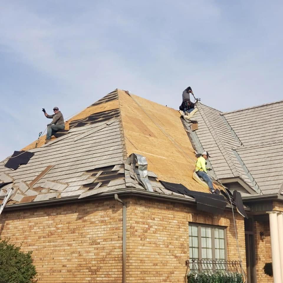 A Tops Roofing crew tearing old shingles down to the wood decking on a brick home